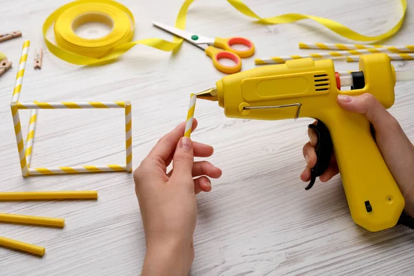 Woman with hot glue gun making craft at white wooden table, closeup