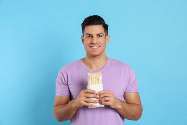 Man with delicious shawarma on turquoise background