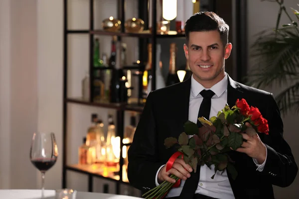 Happy man with roses waiting for his girlfriend in restaurant on Valentine\'s day