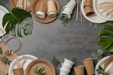 Tek kullanımlık sofra takımı çerçevesi ve gri arka planda farklı yeşil yapraklar. Metin için boşluk