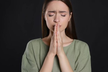 Elleri sımsıkı bağlı bir kadın siyah arka planda dua ediyor.