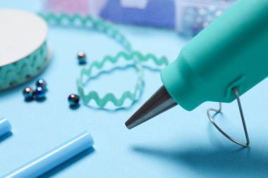 Hot glue gun and handicraft materials on light blue table, closeup