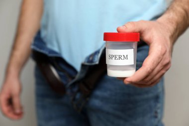 Fermuarsız pantolonlu donör sperm kabını tutuyor, yakın plan.