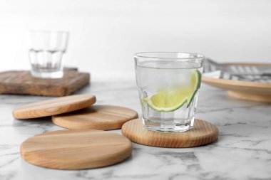 Bir bardak limonata ve beyaz kuliste mermer masanın üzerinde bardak altlığı.