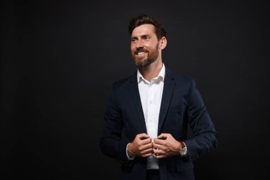 Siyah arka planda takım elbiseli gülümseyen sakallı adamın portresi. Metin için boşluk
