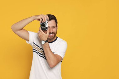 Kameralı adam sarı arkaplanda fotoğraf çekiyor, mesaj için yer var. İlginç bir hobi.