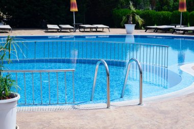 Outdoor swimming pool with ladder and railing on sunny day