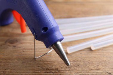 Koyu mavi tutkal tabancası ve sopalar ahşap masaya yakın plan.