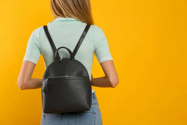 Closeup view of woman with backpack on yellow background, back view. Space for text