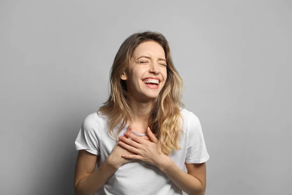 Cheerful young woman laughing on grey background