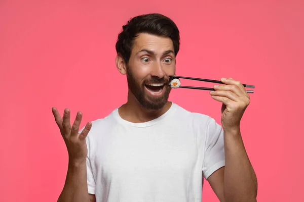 Emocjonalny Mężczyzna Trzyma Smaczne Sushi Roll Pałeczkami Różowym Tle — Zdjęcie stockowe