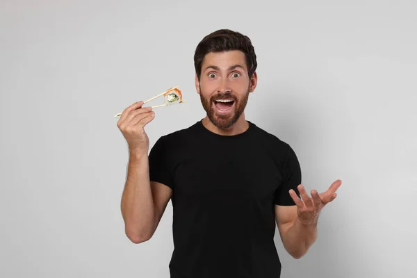 Homem Emocional Segurando Rolo Sushi Com Pauzinhos Fundo Cinza Claro — Fotografia de Stock