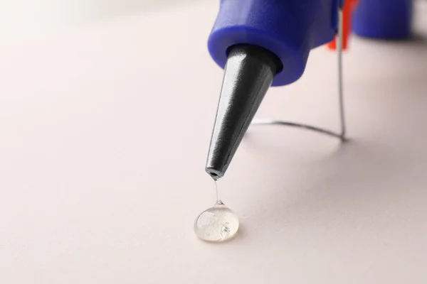 Melted glue dripping from hot gun on white table, closeup. Space for text