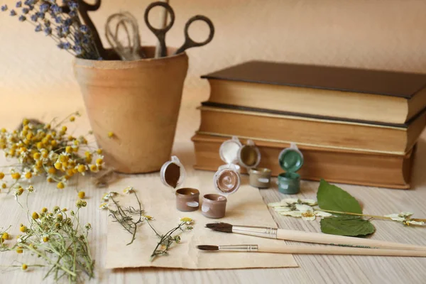 Beautiful dried flowers, books, brushes and paints on wooden table