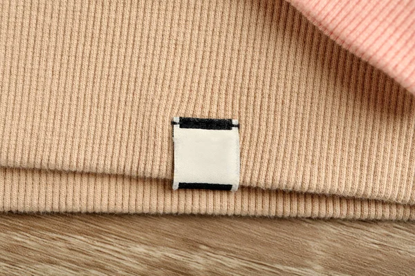 Beige Apparel Blank Clothing Label Wooden Table Top View — Stockfoto