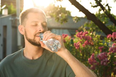 Man drinking water outdoors on hot summer day. Refreshing drink