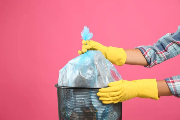 Woman taking garbage bag out of bin on pink background, closeup