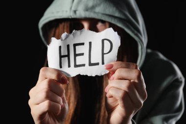 Elinde kelime olan bir kağıt parçası olan bir kadın. Siyah arka planda yardım, yakın plan. Aile içi şiddet kavramı