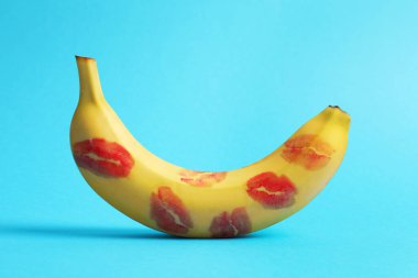 Banana covered with red lipstick marks on light blue background. Potency concept clipart