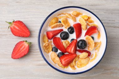 Bowl of tasty crispy corn flakes with milk and berries on wooden table, flat lay