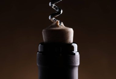 Opening wine bottle with corkscrew on dark brown background, closeup