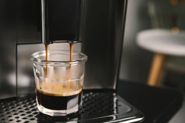 Espresso makinesi bardağa kahve dolduruyor. Arka plan bulanık, yakın plan. Metin için boşluk
