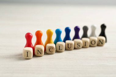 Colorful pawns and cubes with word Inclusion on white wooden table