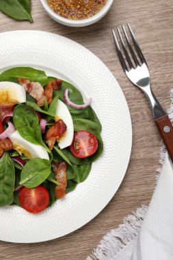 Delicious salad with boiled egg, bacon and vegetables served on wooden table, flat lay