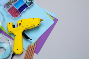 Sıcak tutkal tabancası ve el işi malzemesi gri arka planda, düz yerde. Metin için boşluk