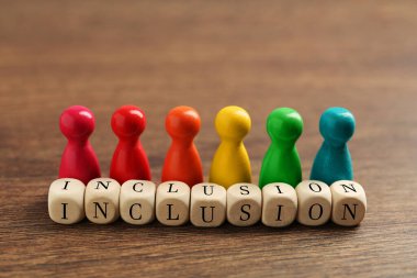 Colorful pawns and cubes with word Inclusion on wooden table, closeup