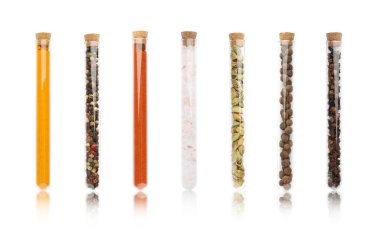 Beyaz zemin üzerinde farklı baharatlar bulunan cam tüpler.