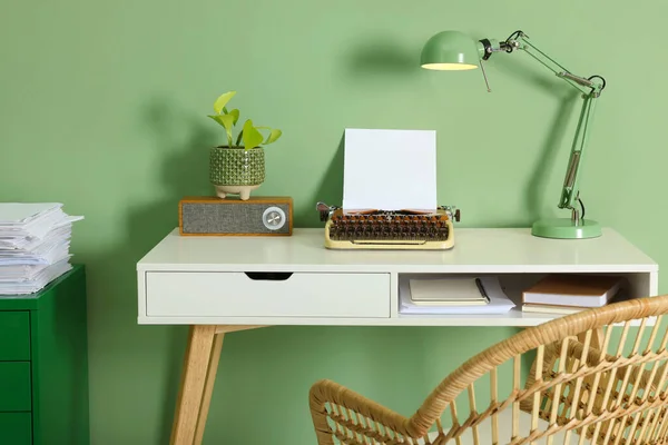 Writer's workplace with typewriter on wooden desk near pale green wall in room