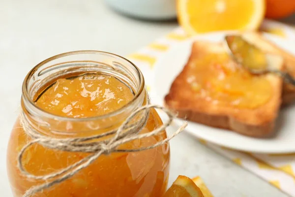 Delicious orange marmalade in glass jar on light table, closeup. Space for text