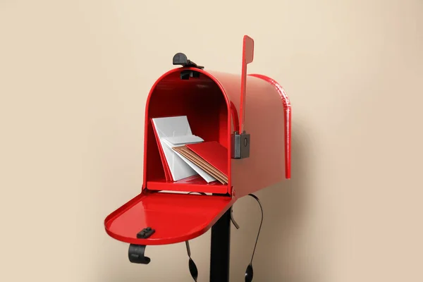 Open red letter box with envelopes against beige background