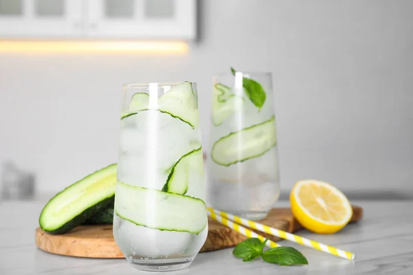 Tasty fresh cucumber water, sliced lemon and basil on white marble table indoors