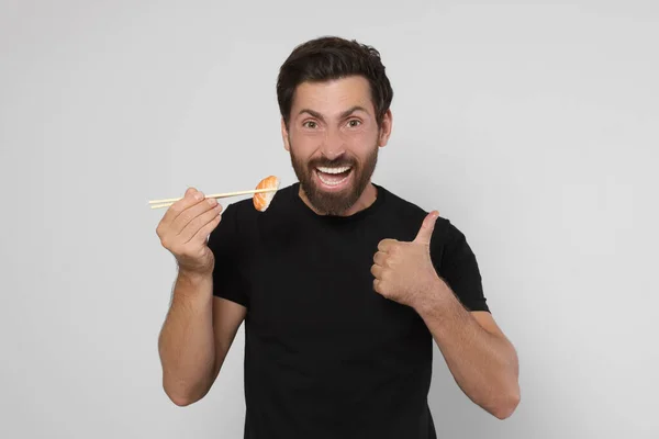 Emotional Man Holding Tasty Sushi Chopsticks Showing Thumbs Light Grey — Stock Photo, Image