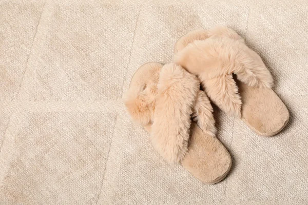 Fluffy beige slippers on soft carpet, space for text