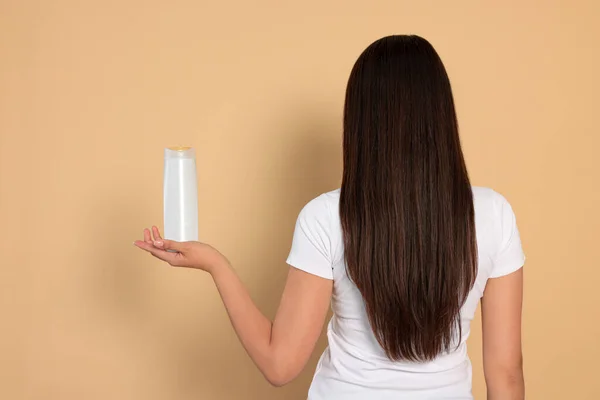 Young Woman Holding Bottle Shampoo Beige Background Back View — Stock Photo, Image