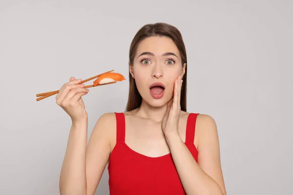 Joven Mujer Emocional Sosteniendo Sushi Con Palillos Sobre Fondo Claro — Foto de Stock