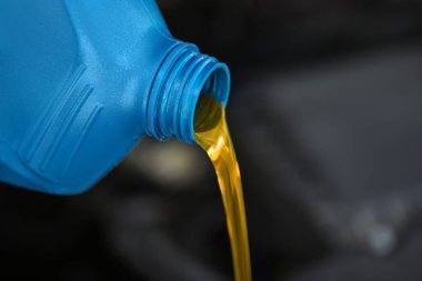 Mavi konteynırdan bulanık arka plana motor yağı dökülüyor, yakın plan. Metin için boşluk