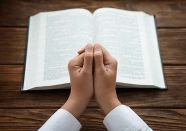 İncil 'le ahşap masada dua ederken el ele tutuşan kadın, yakın plan.
