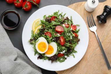 Delicious salad with boiled egg, arugula and tomatoes served on black table, flat lay