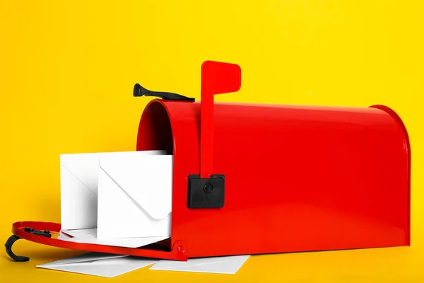 Open red letter box with envelopes on yellow background, closeup