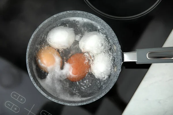 Boiling chicken eggs in saucepan on electric stove, top view