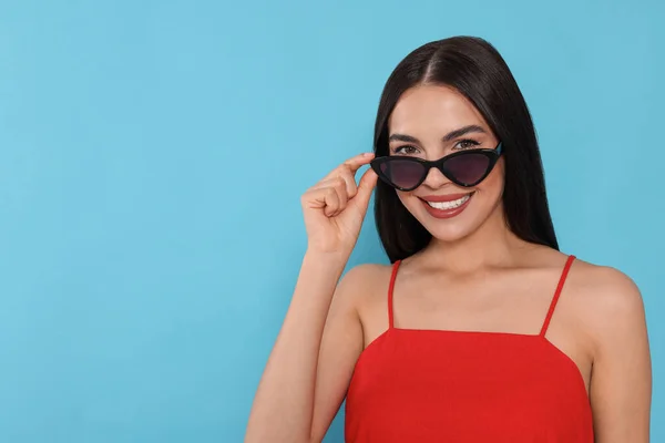 Aantrekkelijke Vrolijke Vrouw Die Modieuze Zonnebrillen Tegen Lichtblauwe Achtergrond Aanraakt — Stockfoto