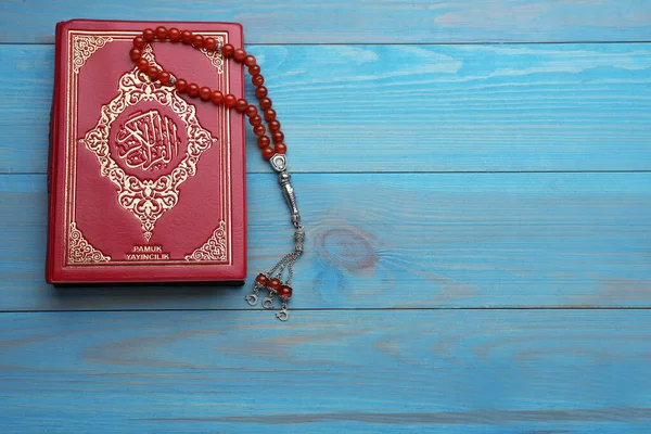 Muslim prayer beads and Quran on light blue wooden table, top view. Space for text