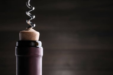 Opening wine bottle with corkscrew on dark background, closeup. Space for text