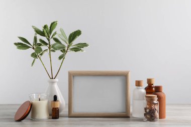 Boş fotoğraf çerçevesi, farklı şişeler ve ahşap masada dekor elementleri.