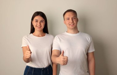 Mutlu genç kadın ve erkek portresi açık arkaplanda baş parmak gösteriyor.