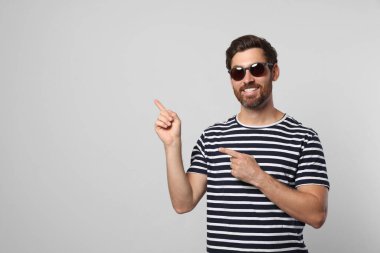 Açık gri arka planda şık güneş gözlüklü, gülümseyen sakallı adamın portresi. Metin için boşluk